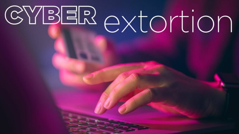 Close-up of a person holding a smartphone and typing on a laptop keyboard with the text "cyber extortion" in the background, as the screen emits an urgent beep.